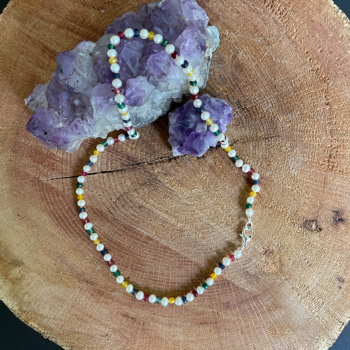 Multicolored Jade and white Pearl necklace on a wooden surface with amethyst crystals