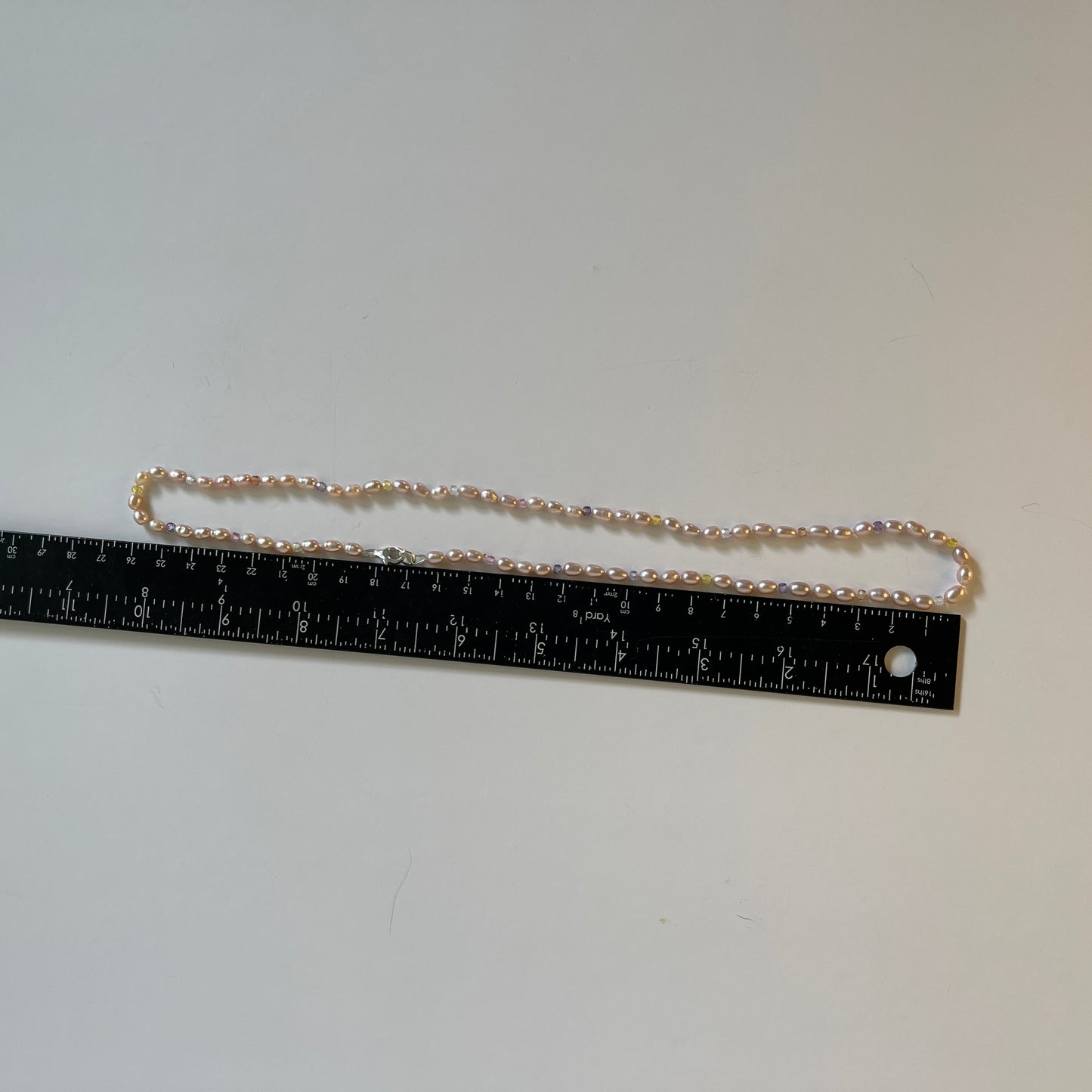 Pink Pearl and multicolored  cubic zirconia necklace on white background with ruler