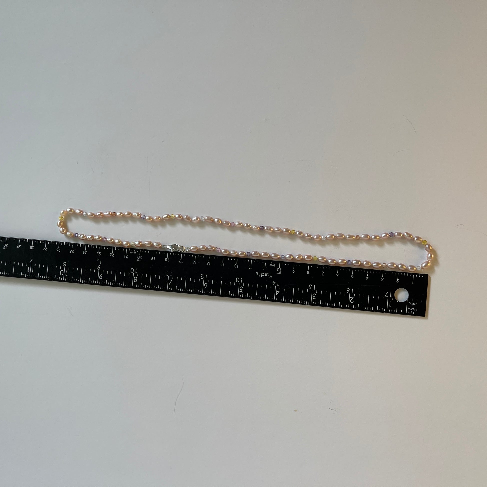 Pink Pearl and multicolored  cubic zirconia necklace on white background with ruler