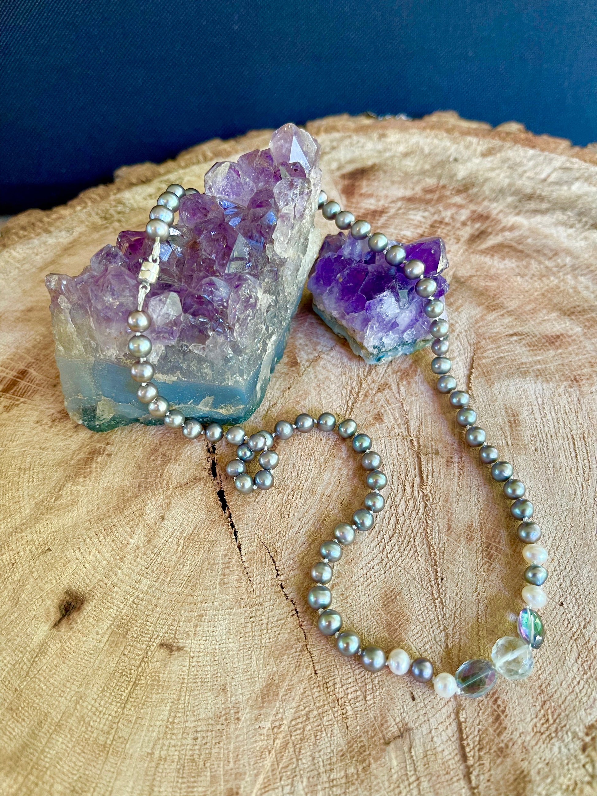 Necklace of Silver Peacock pearls with  Aquamarine and Rainbow Tourmaline focus beads on a wooden surface
