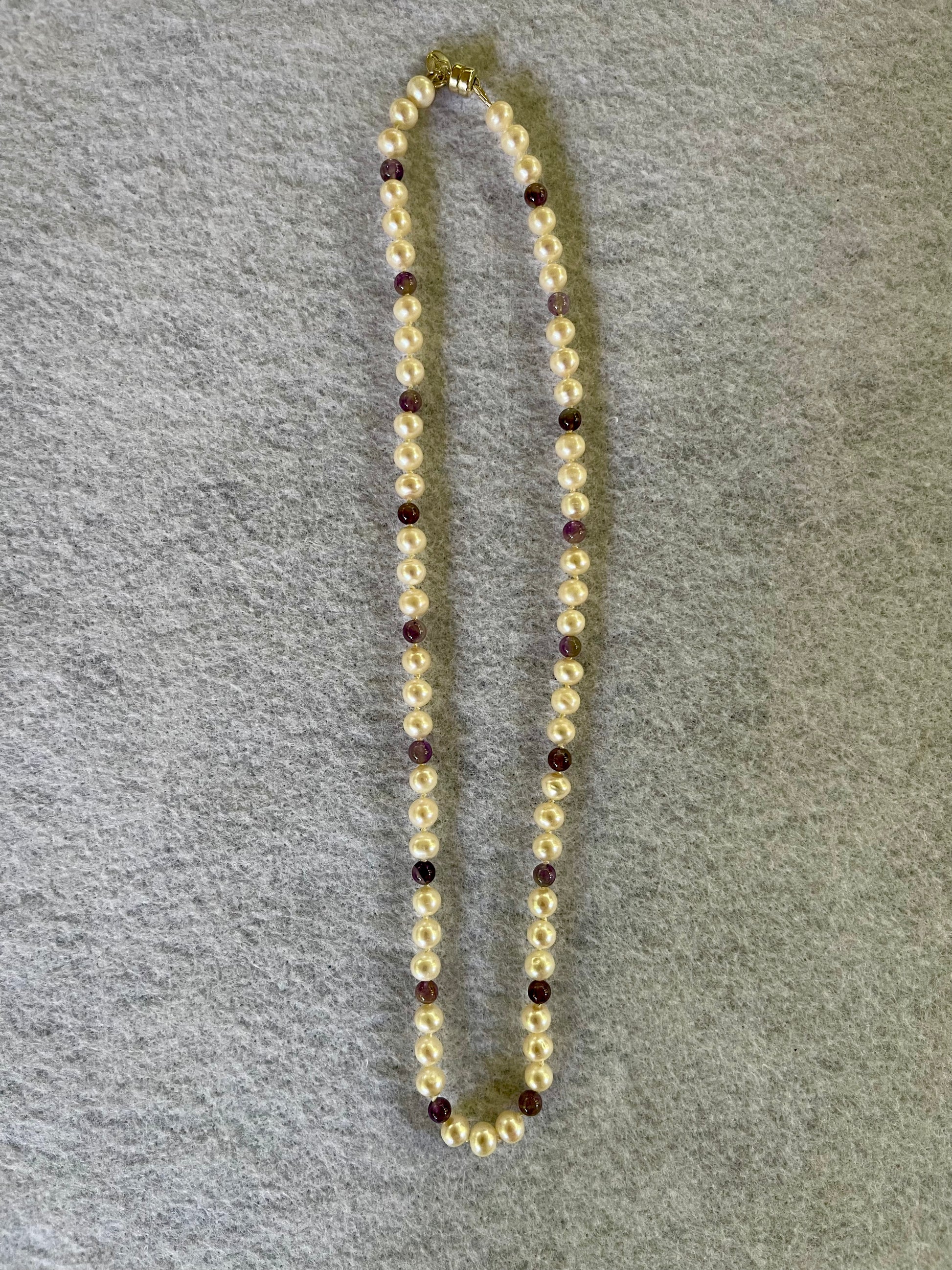 Beaded necklace with alternating white Pearls and Amethyst beads on a gray surface