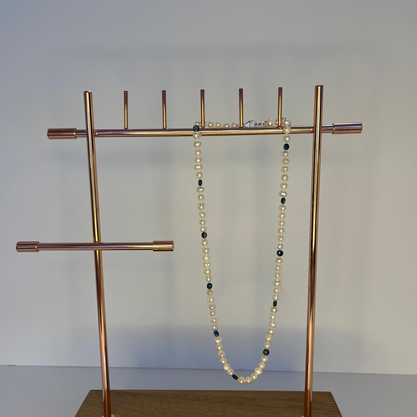 Gold jewelry stand with a Pearl and Blue Jasper necklace on a plain background