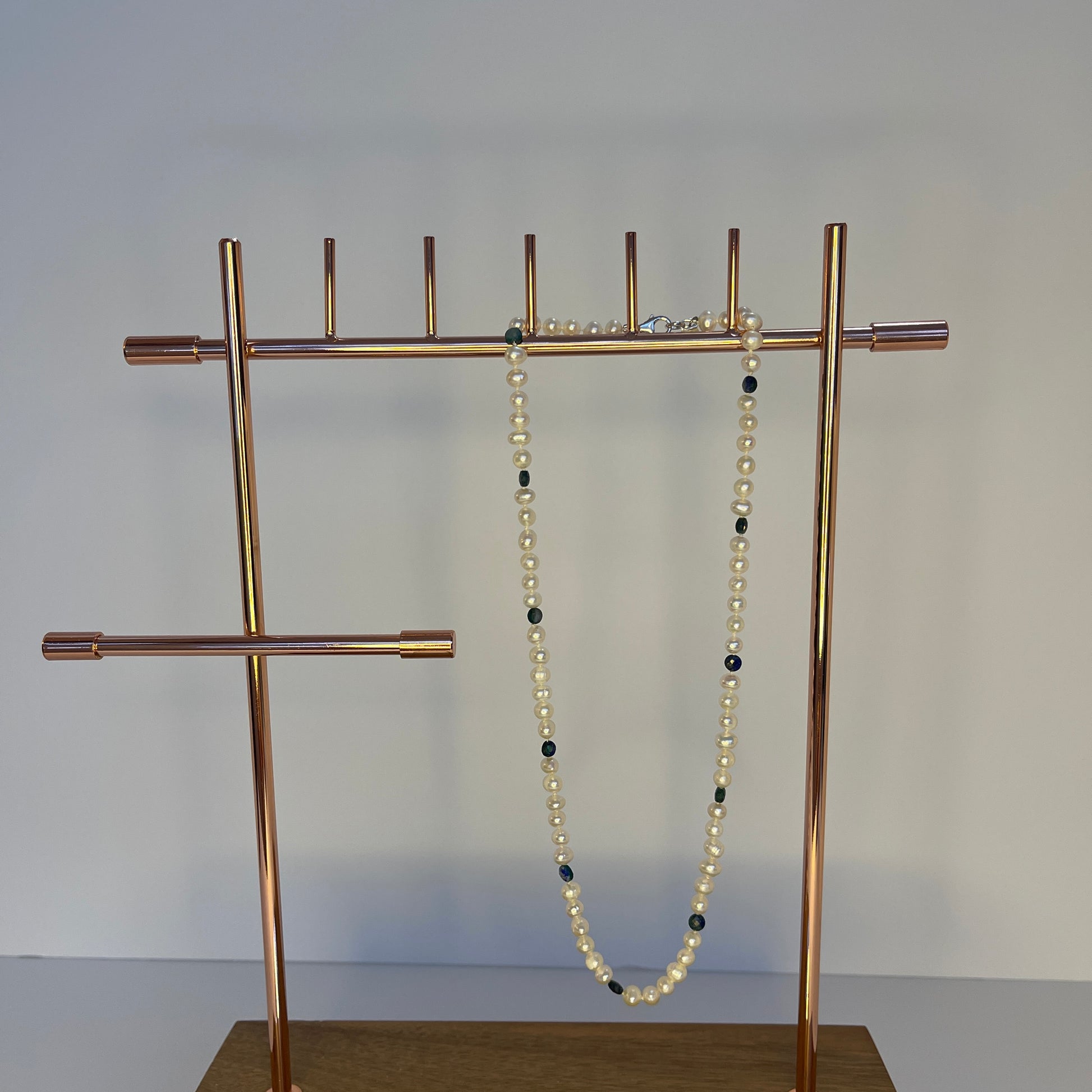 Gold jewelry stand with a Pearl and Blue Jasper necklace on a plain background