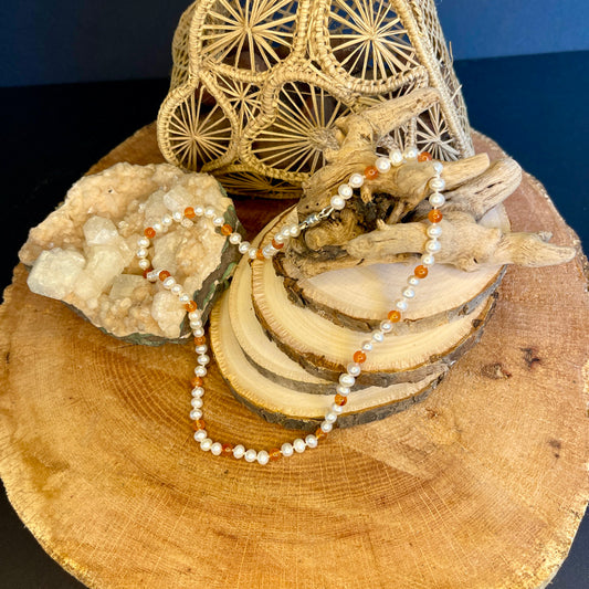Necklace with white pearls and orange carnelian beads on a wooden surface with natural elements