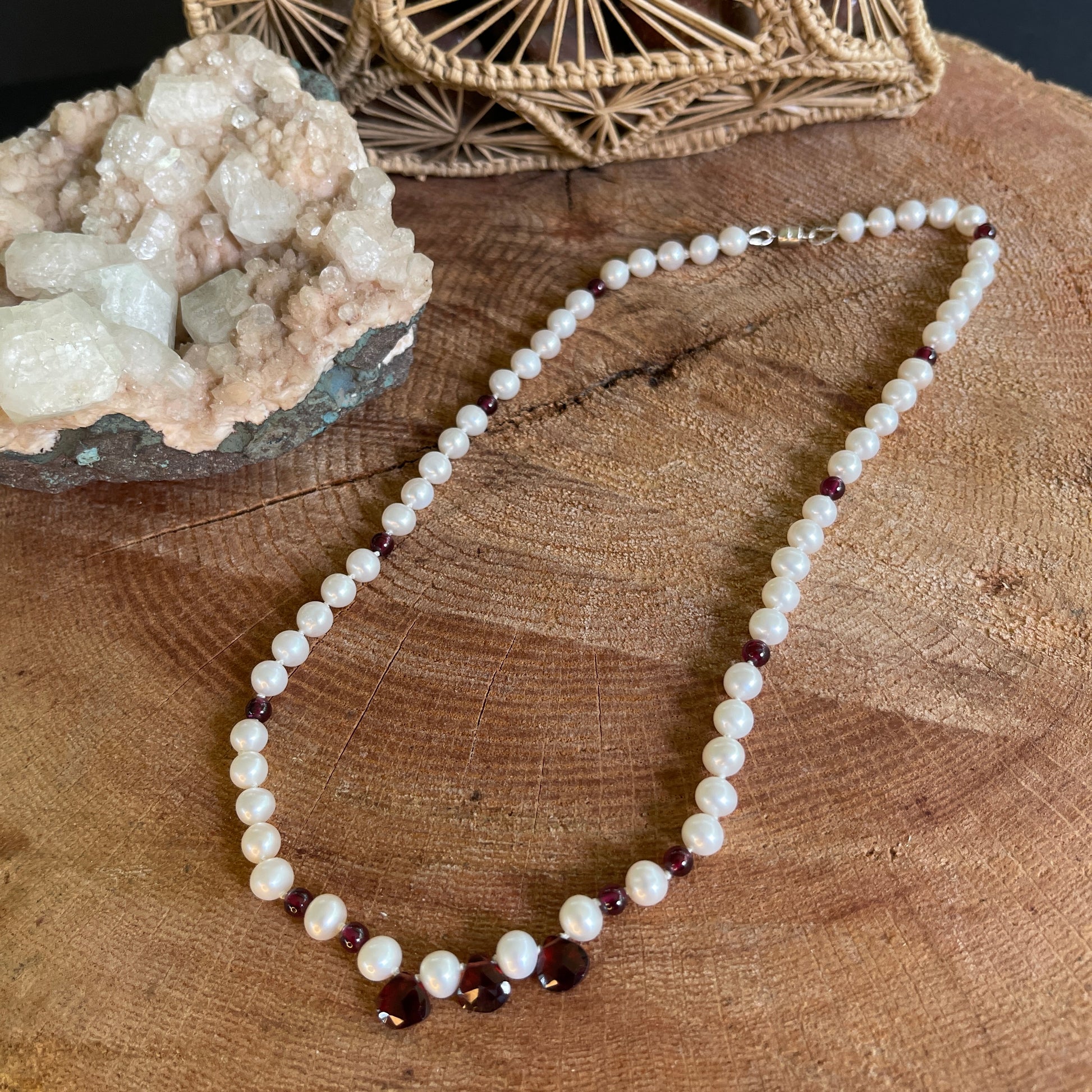 Pearl and Garnet bead necklace  with teardrops on a wooden surface with decorative elements.