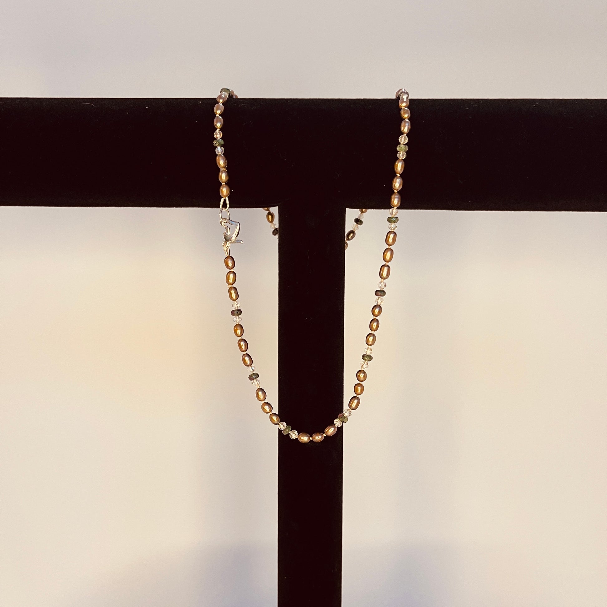 Chocolate brown Pearls with crystals and green jasper necklace hanging from a black bar against a neutral background