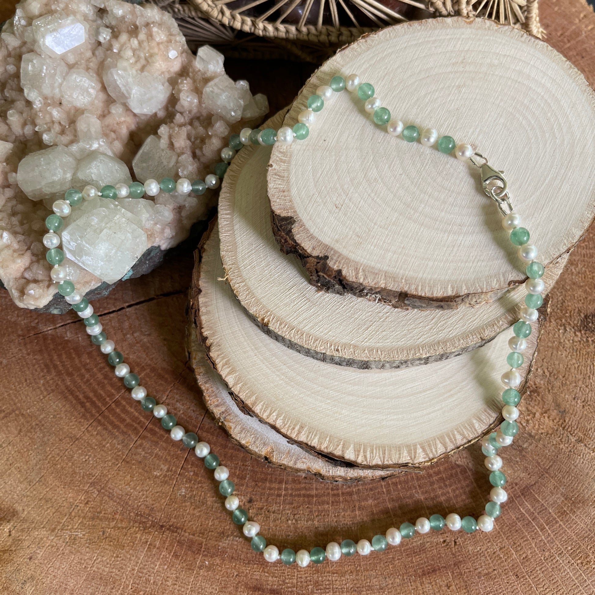 Necklace with green aventurine beads and white freshwater Pearls on a wooden surface with crystals and natural wood slices.