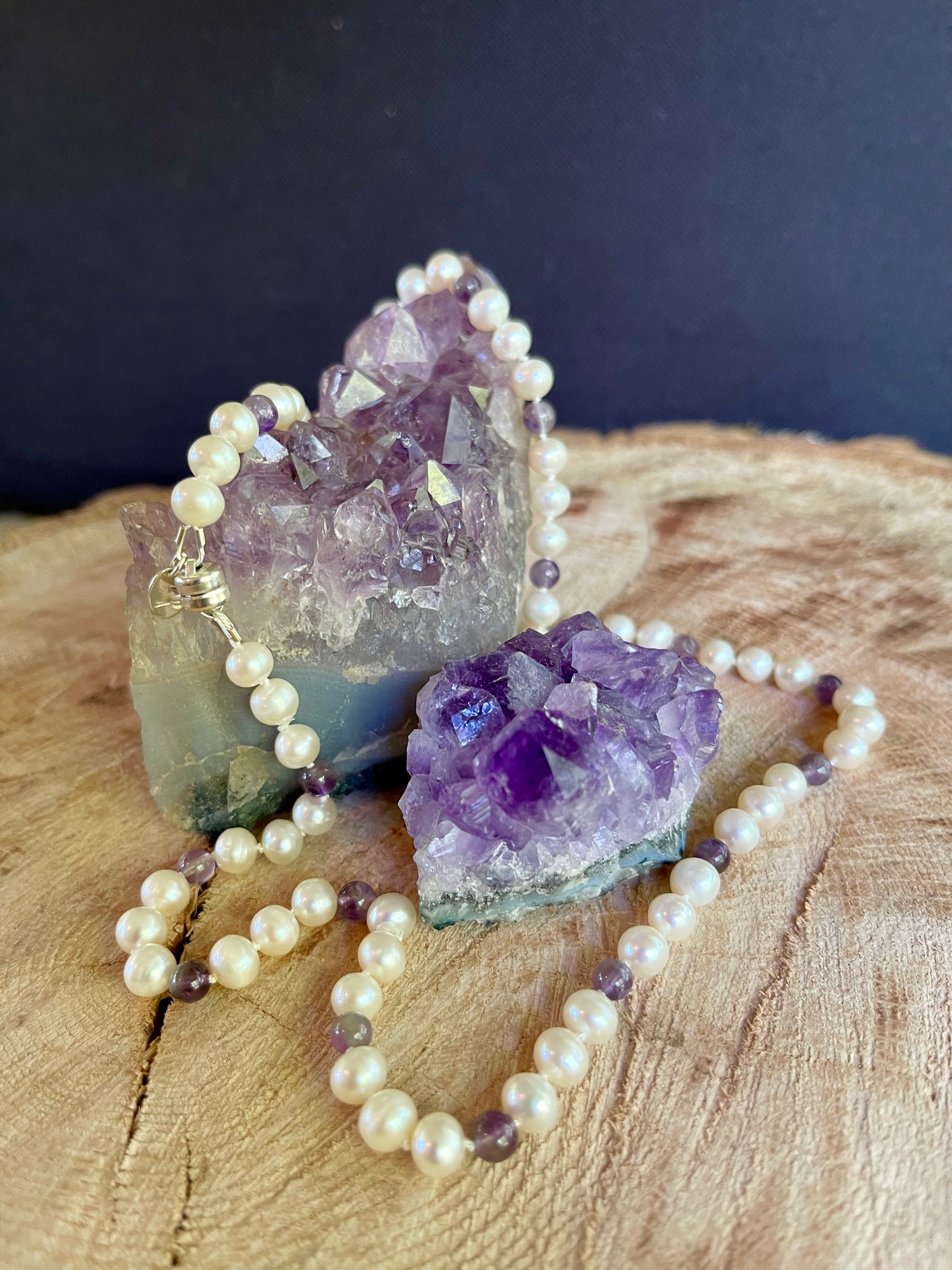 Pearl  and Amethyst beaded necklace with purple amethyst crystal on a wooden surface