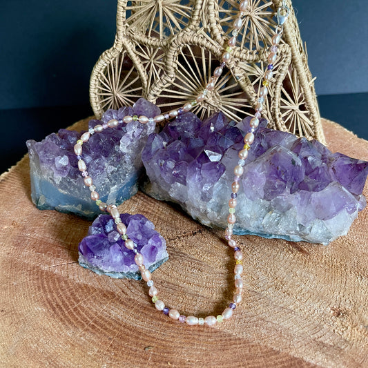 Necklace with mauve Pearls and multicolored cubic Ziconia stones on a wooden surface with amethyst crystals and woven decorative item.