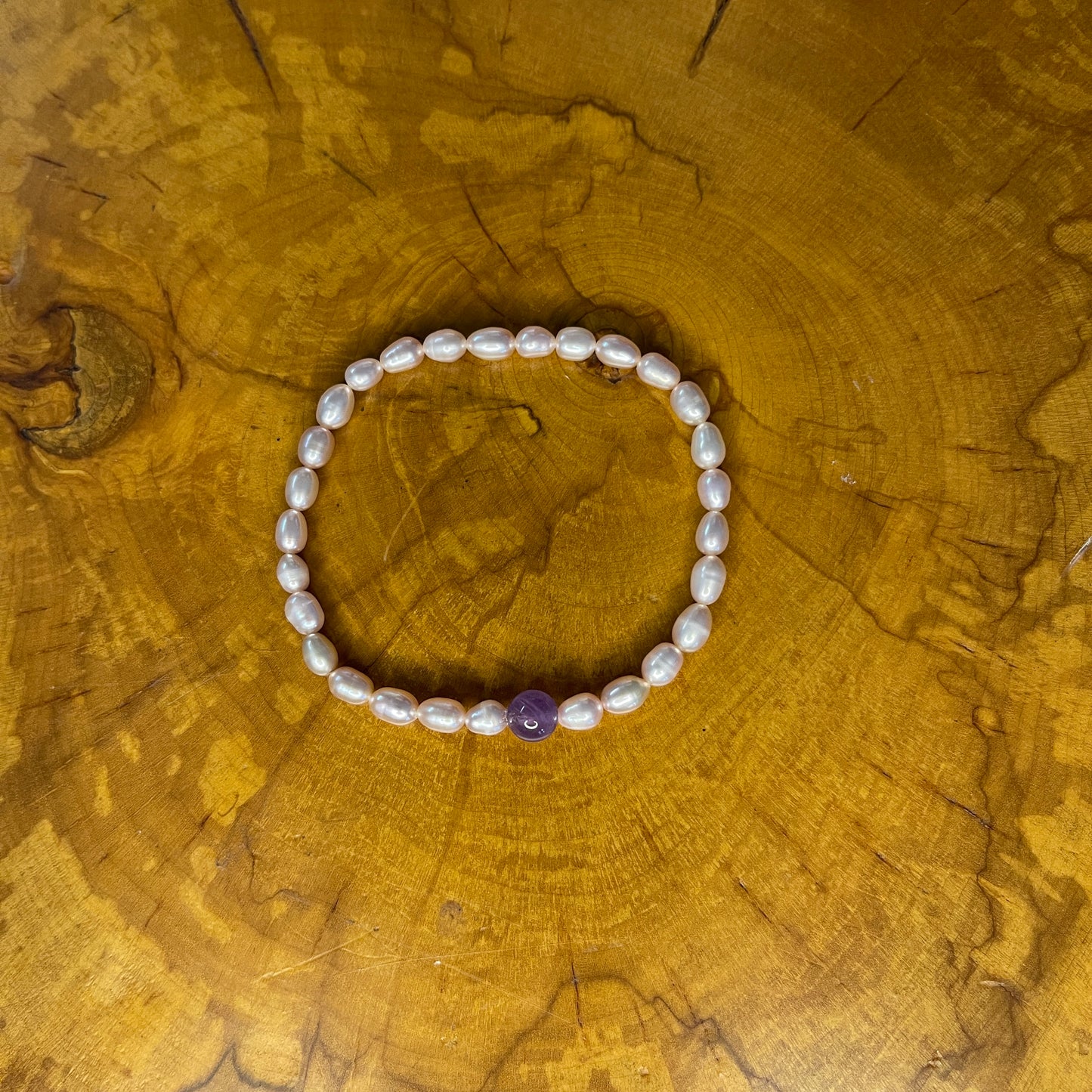 Mauve freshwater Rice  Pearls with Amethyst focus bead on elastic, 7 1/4" on a wooden surface