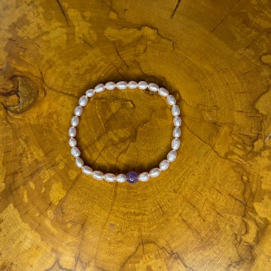 Mauve freshwater Rice  Pearls with Amethyst focus bead on elastic, 7 1/4" on a wooden surface