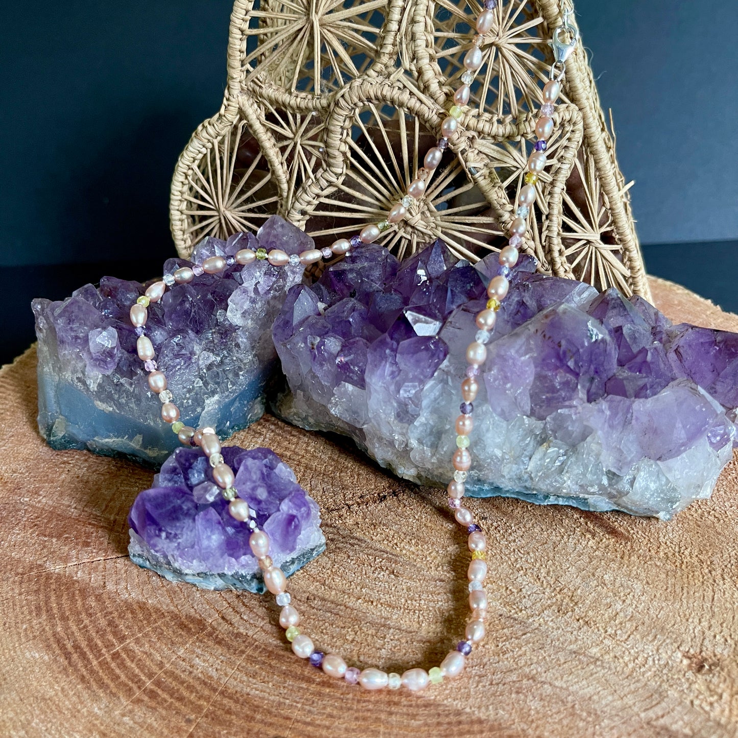 Necklace with purple stones on a wooden surface with amethyst crystals and decorative elements.