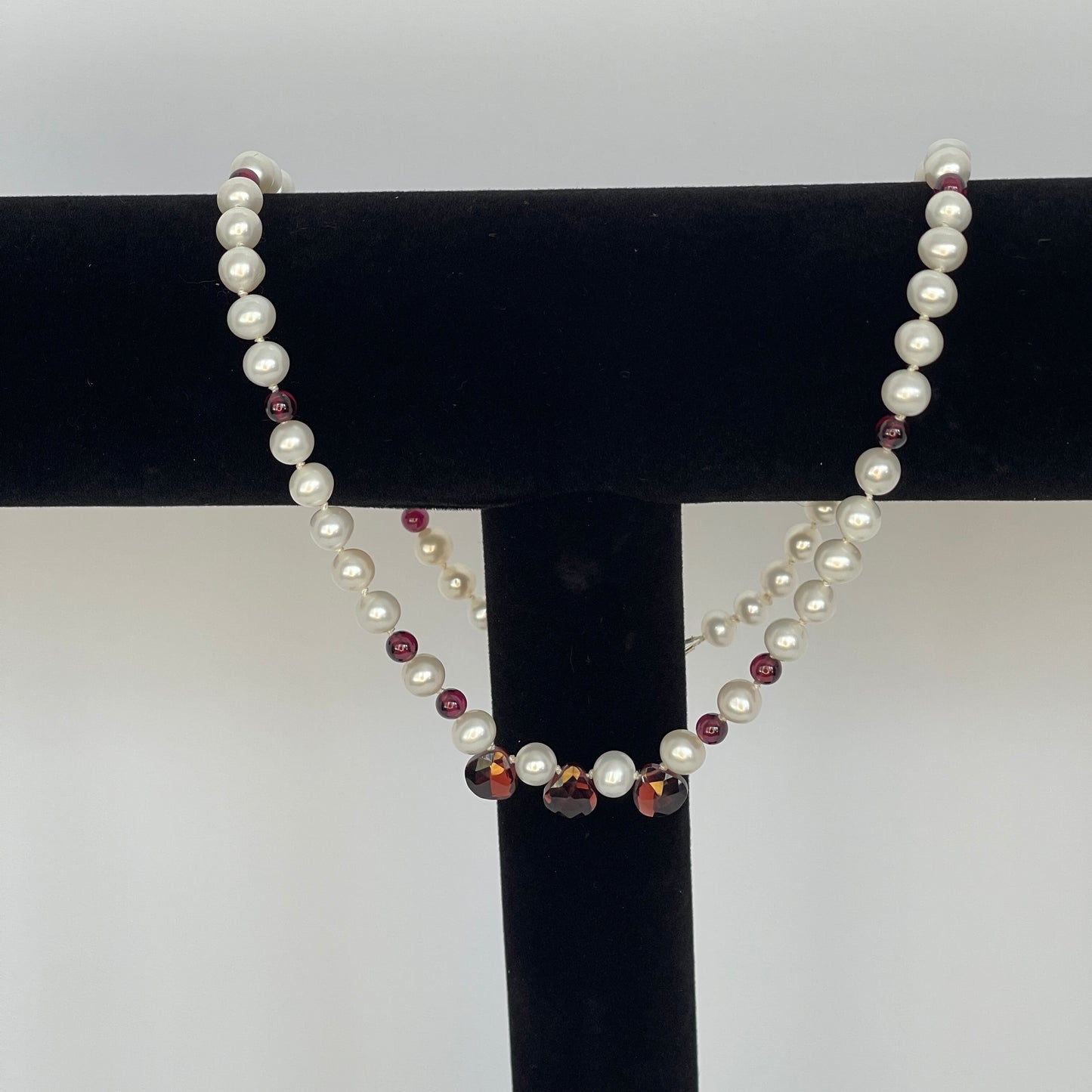 Necklace of White pearls and Garnet beads  and teardrops on a black stand against a white background