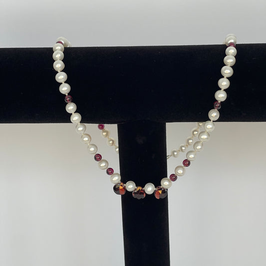 Necklace of White pearls and Garnet beads  and teardrops on a black stand against a white background