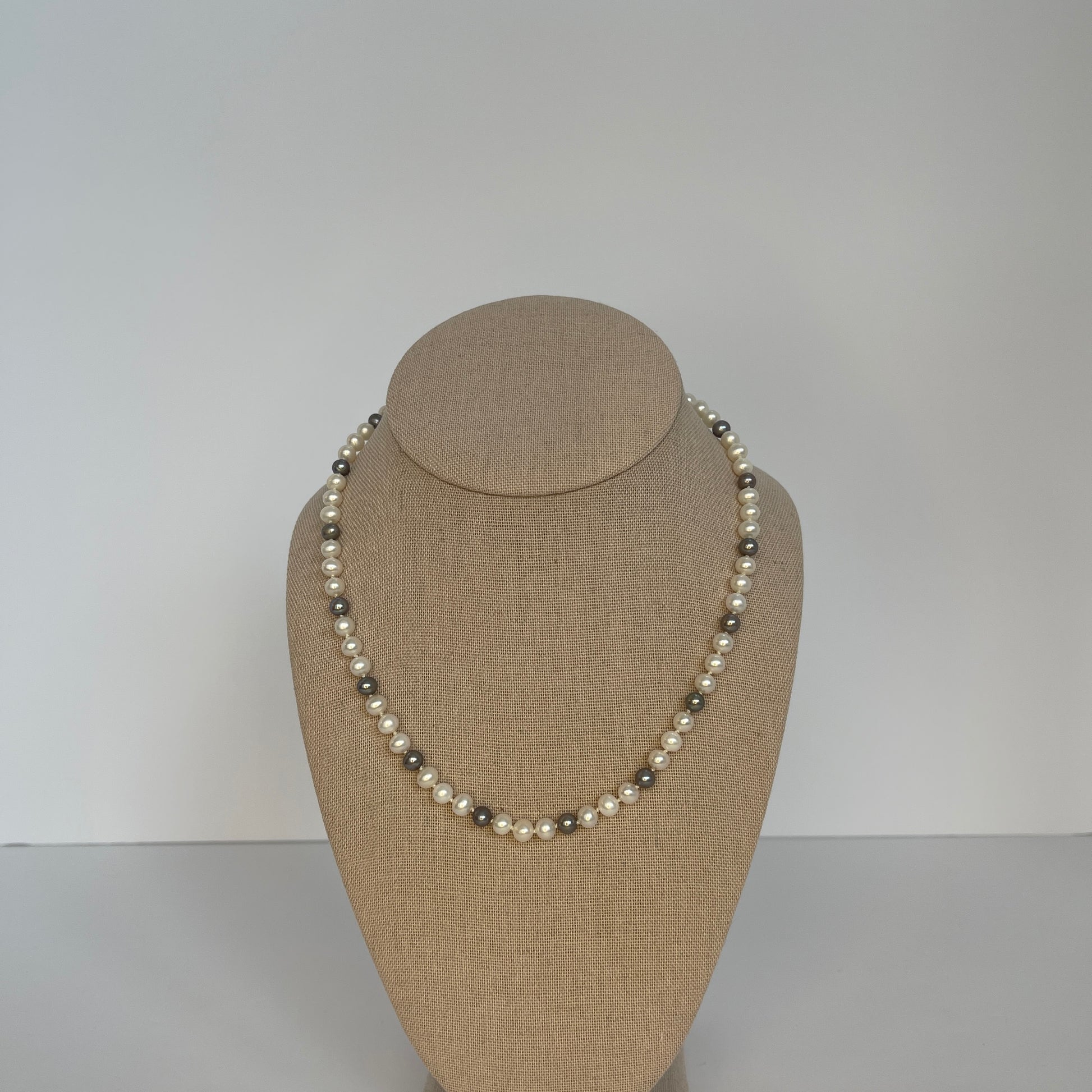 White and Silver Pearl necklace on a mannequin bust against a plain background