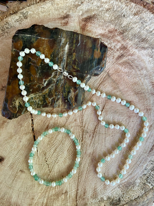 White Pearl and green aventurine beaded necklace and bracelet set on wooden slab with decorative elements