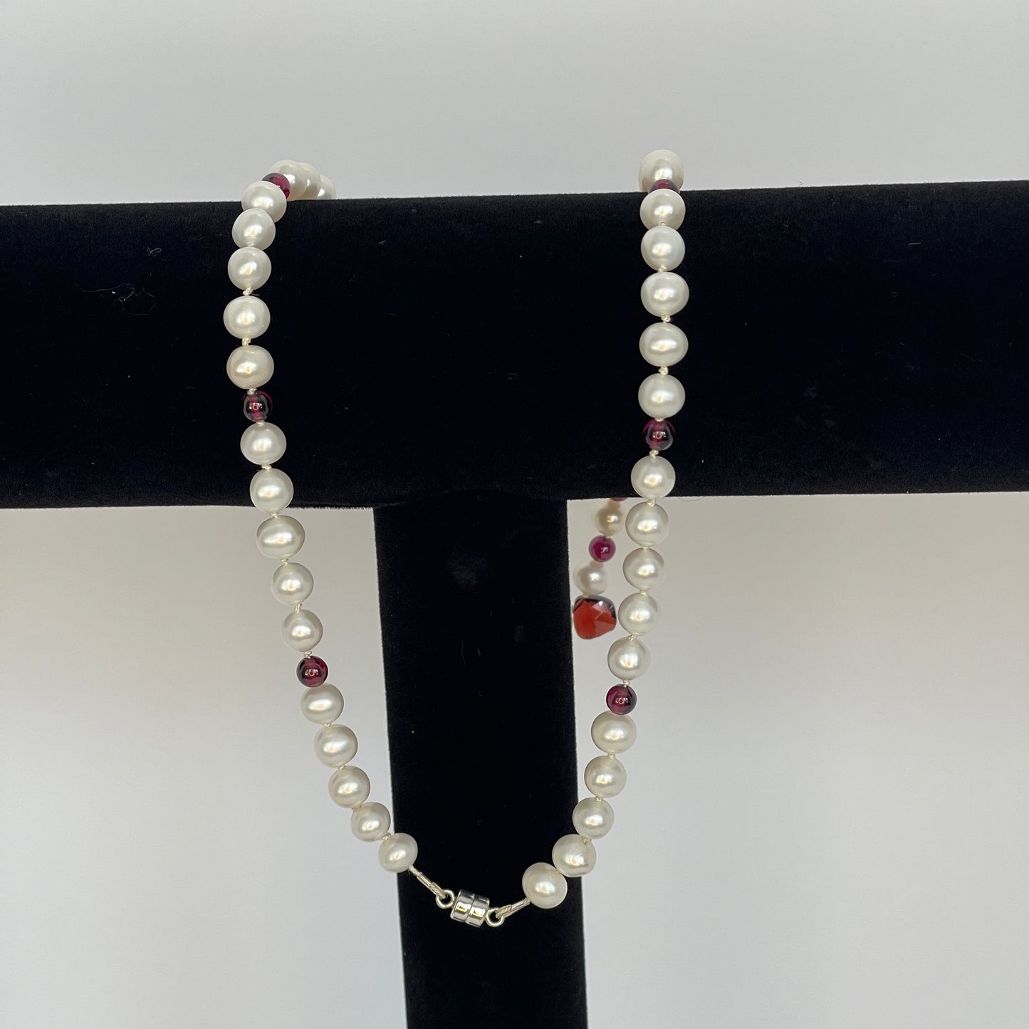 Necklace of White pearls and Garnet beads  and teardrops  showing magnet clasp on a black stand against a white background