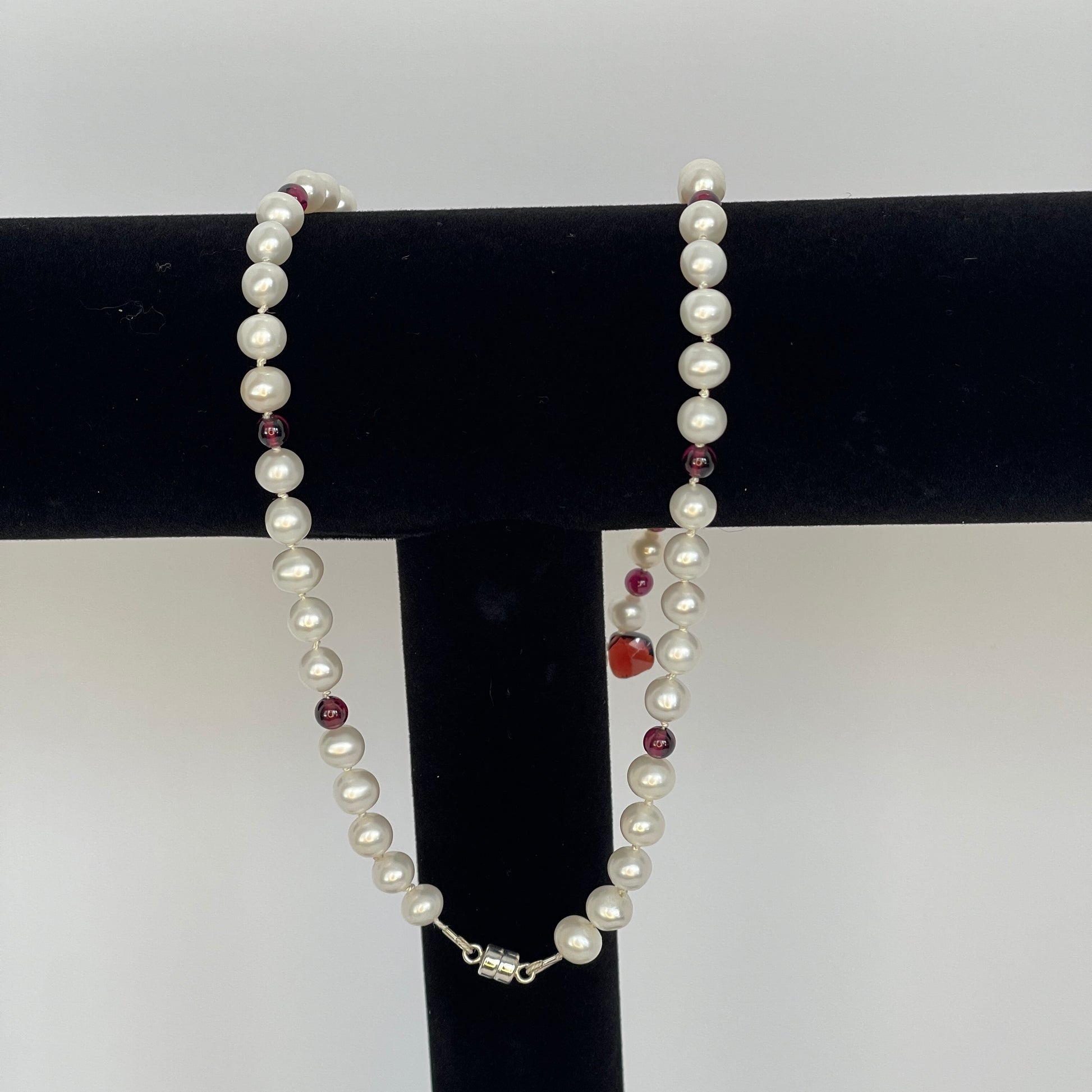 Necklace of White pearls and Garnet beads  and teardrops  showing magnet clasp on a black stand against a white background