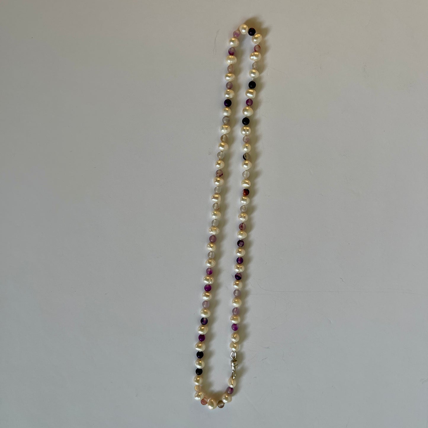 Pearl necklace with purple jasper beads on a plain background