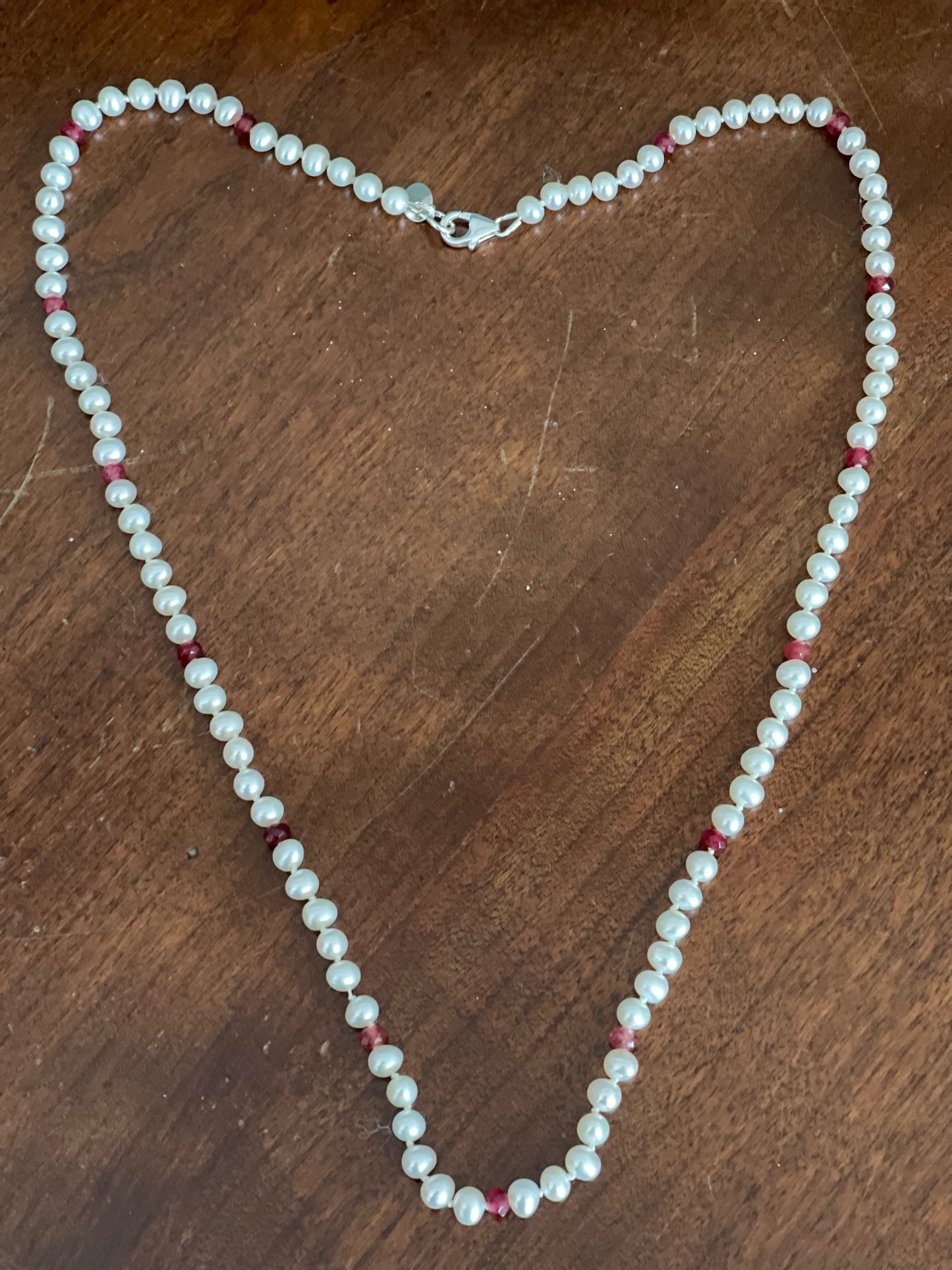 Pearl necklace with red  cubic zirconia accents on a wooden surface