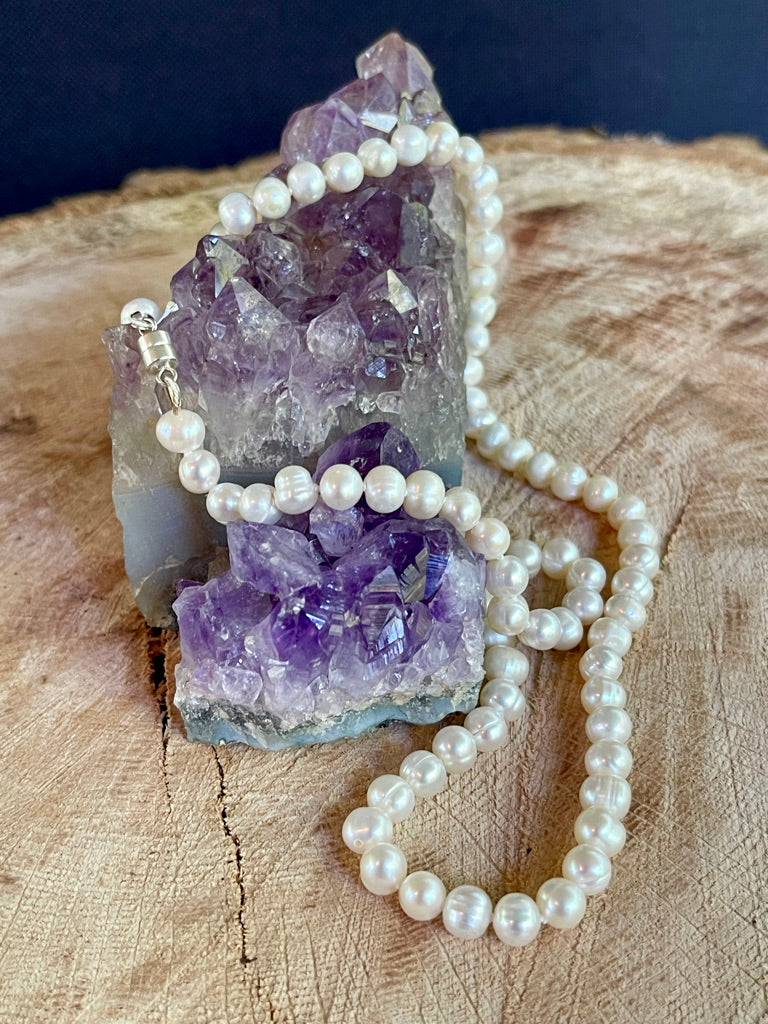 Pearl necklace draped over an amethyst crystal on a wooden surface
