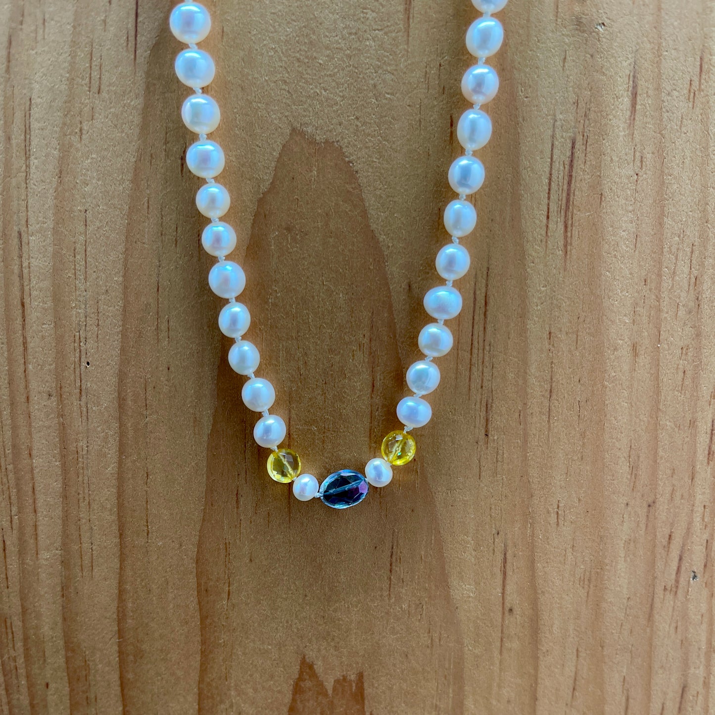 Pearl necklace with citrine and rainbow tourmaline accents on a wooden surface