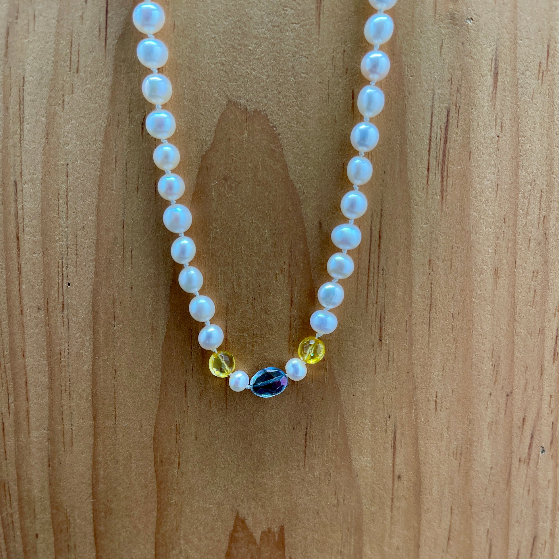 Pearl necklace with citrine and rainbow tourmaline accents on a wooden surface