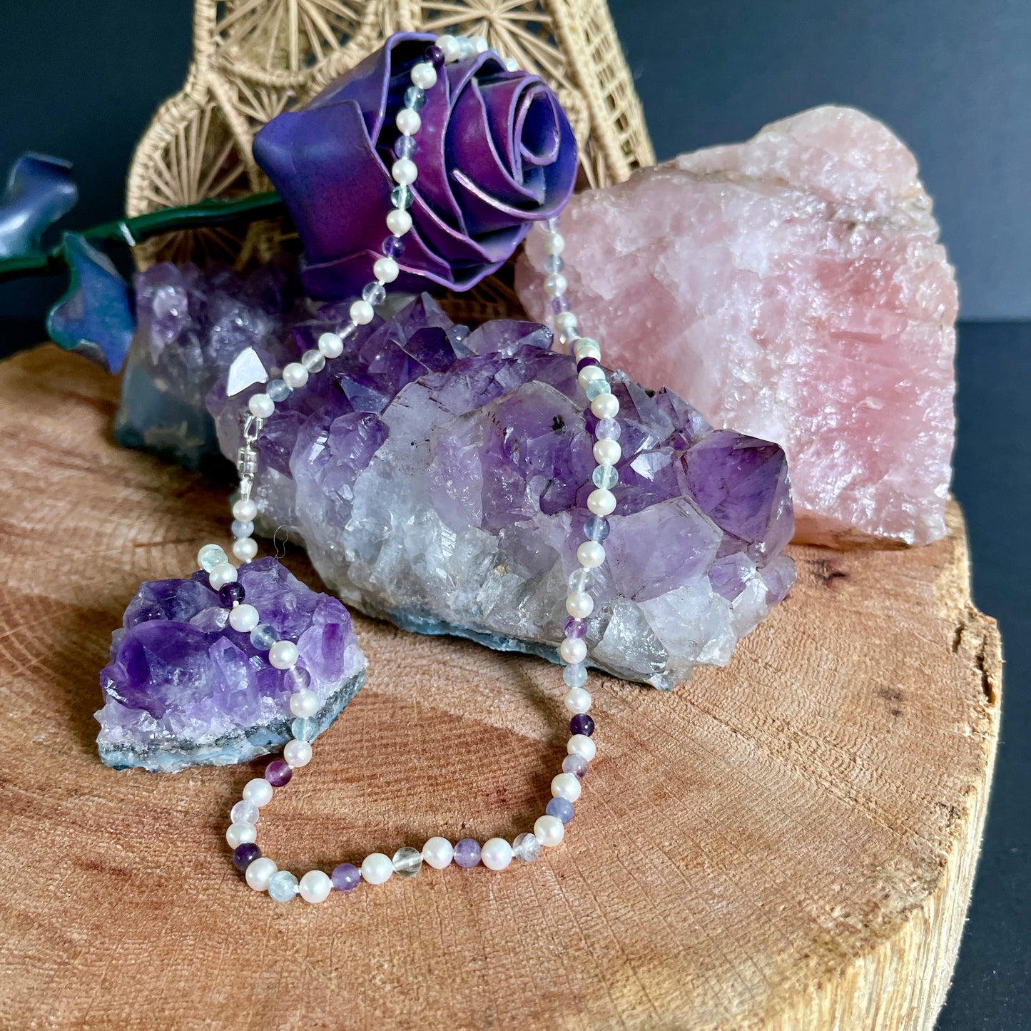 Necklace with White pearls and Fluorite beads on a wooden surface with crystals and a purple rose.