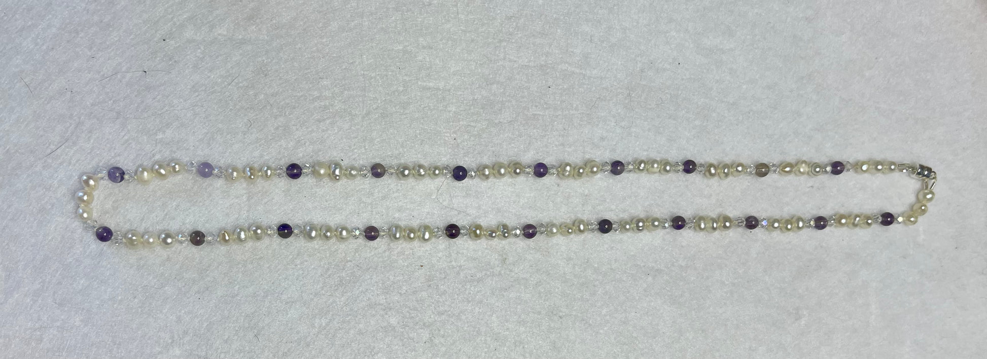 Necklace with white Pearls, Amethyst and crystals on a white surface