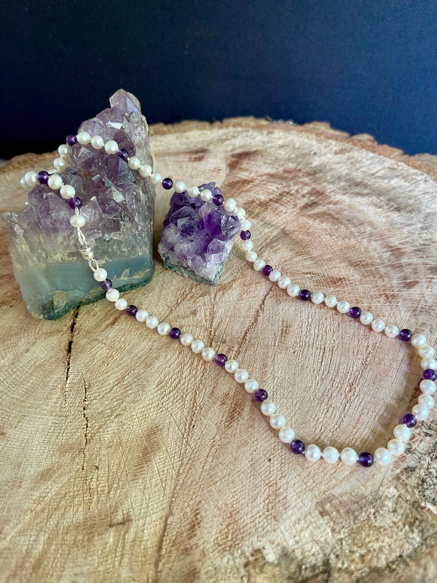 Necklace with White Pearls and Amethyst beads on a wooden surface with crystals