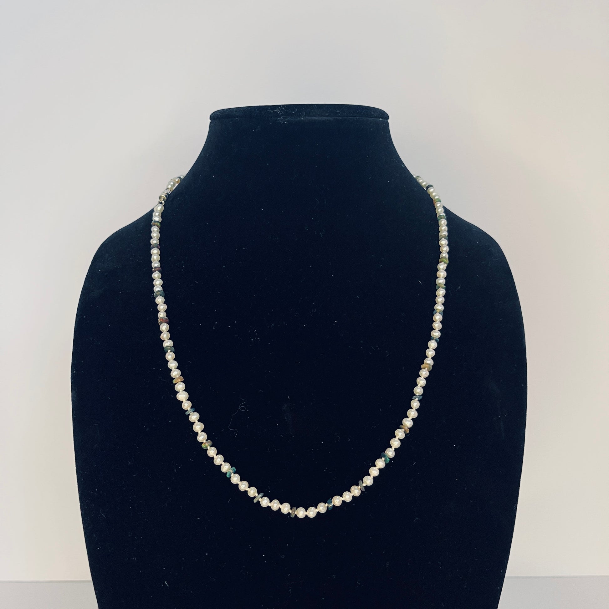 Pearl  and Black Opal necklace on a black velvet stand against a white background