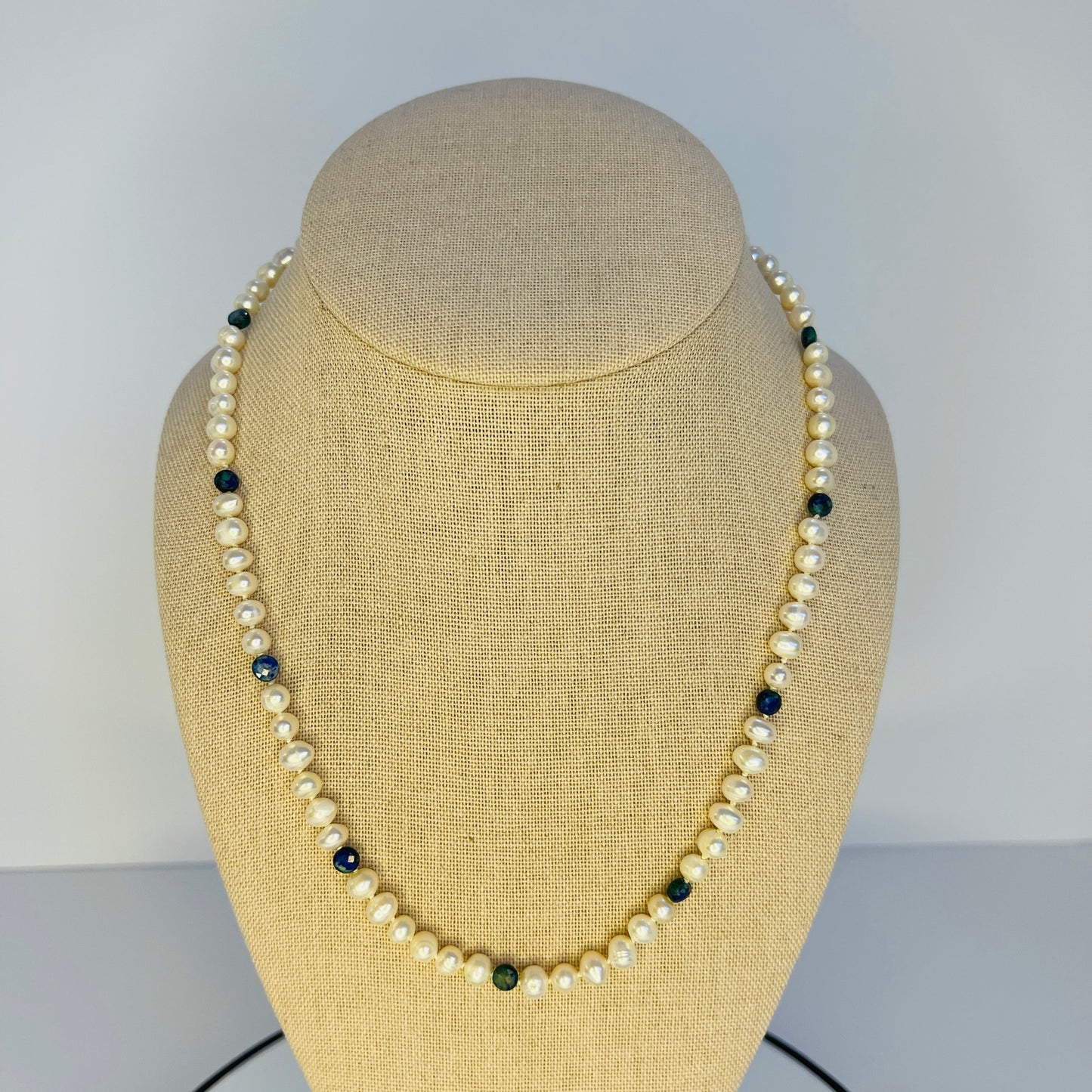 Pearl necklace with black and green beads on a beige mannequin bust against a plain background