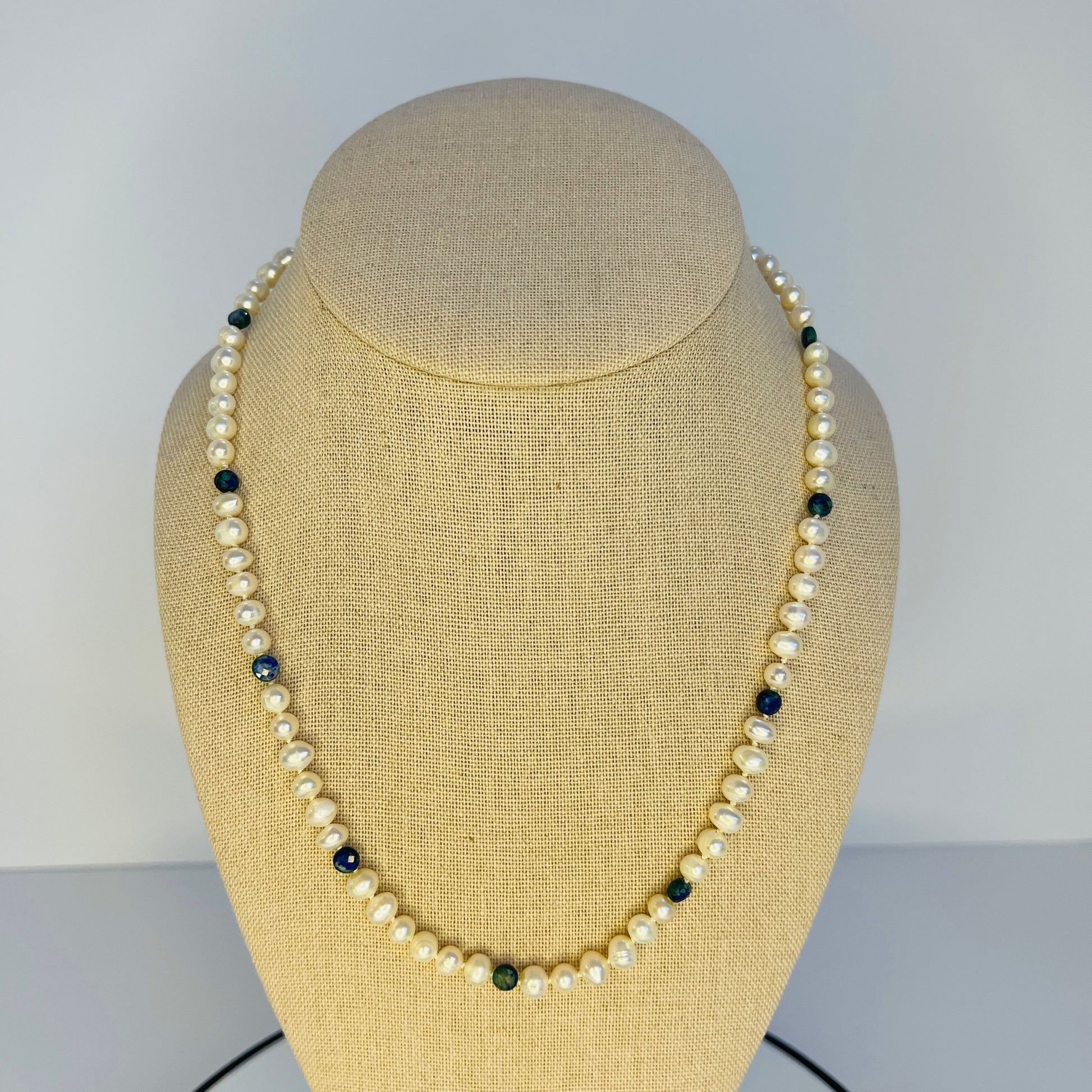 Pearl necklace with black and green beads on a beige mannequin bust against a plain background