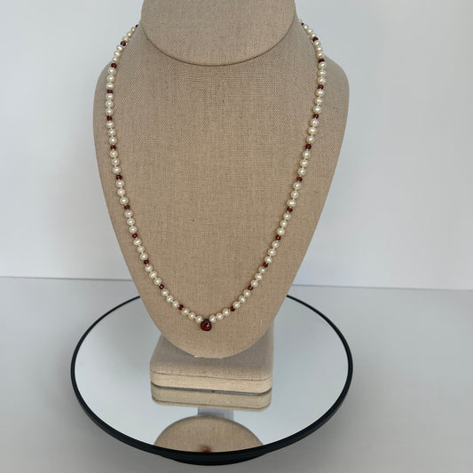 Pearl necklace with red cubic zirconia beads  and one teardrop on a beige mannequin bust against a white background