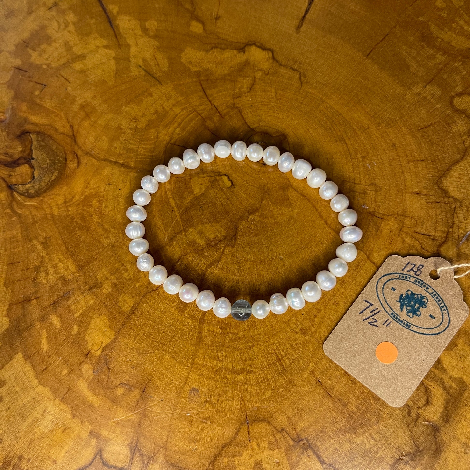 Freshwater White Pearls with Fluorite focus bead on elastic, 7 1/2" on wooden surface with tag