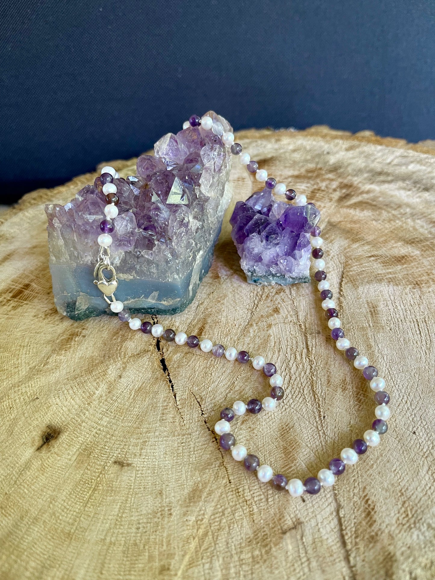 Necklace with White Pearls and alternating Amethyst beads on a wooden surface with crystal formations.