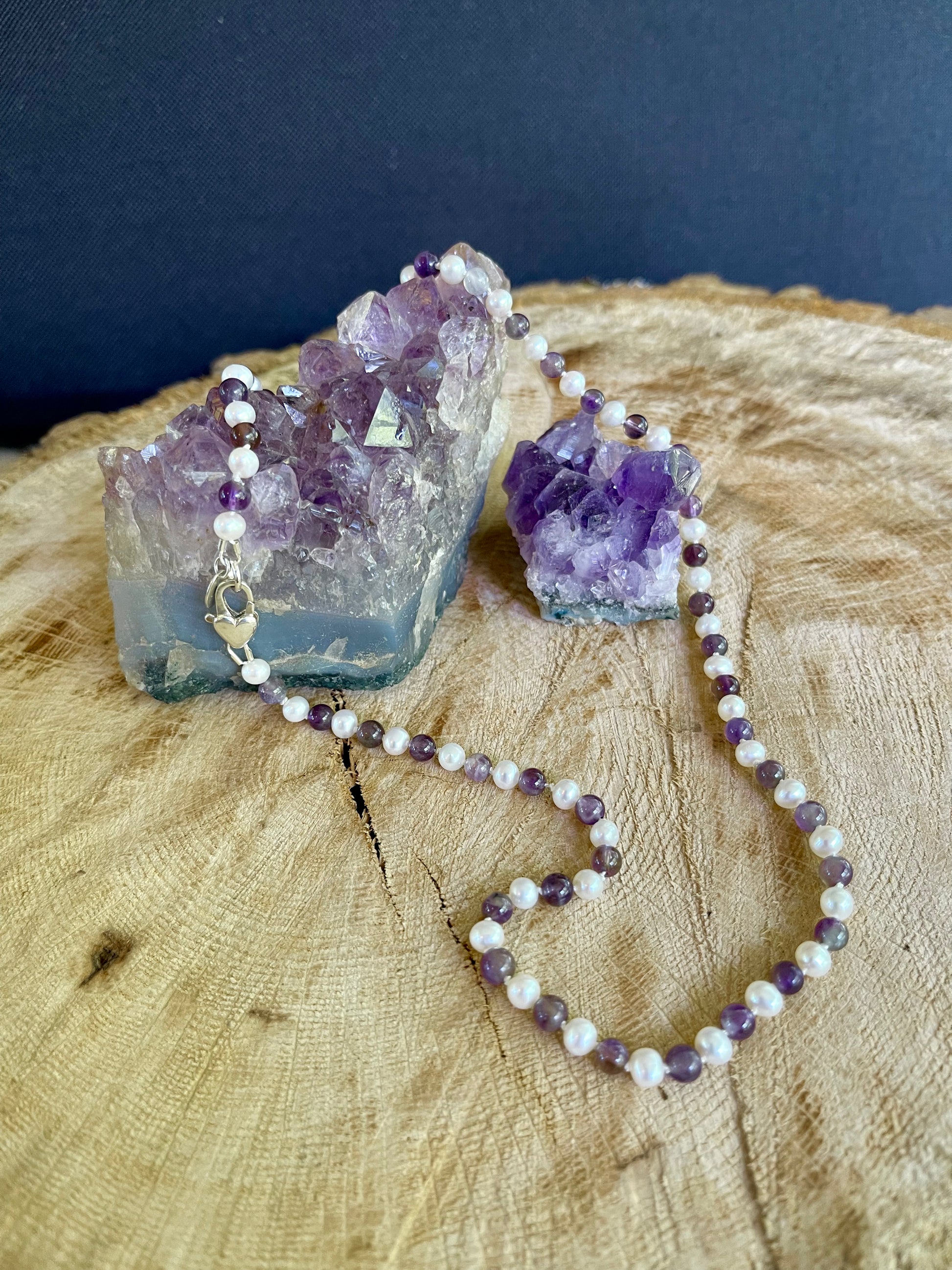 Necklace with White Pearls and alternating Amethyst beads on a wooden surface with crystal formations.