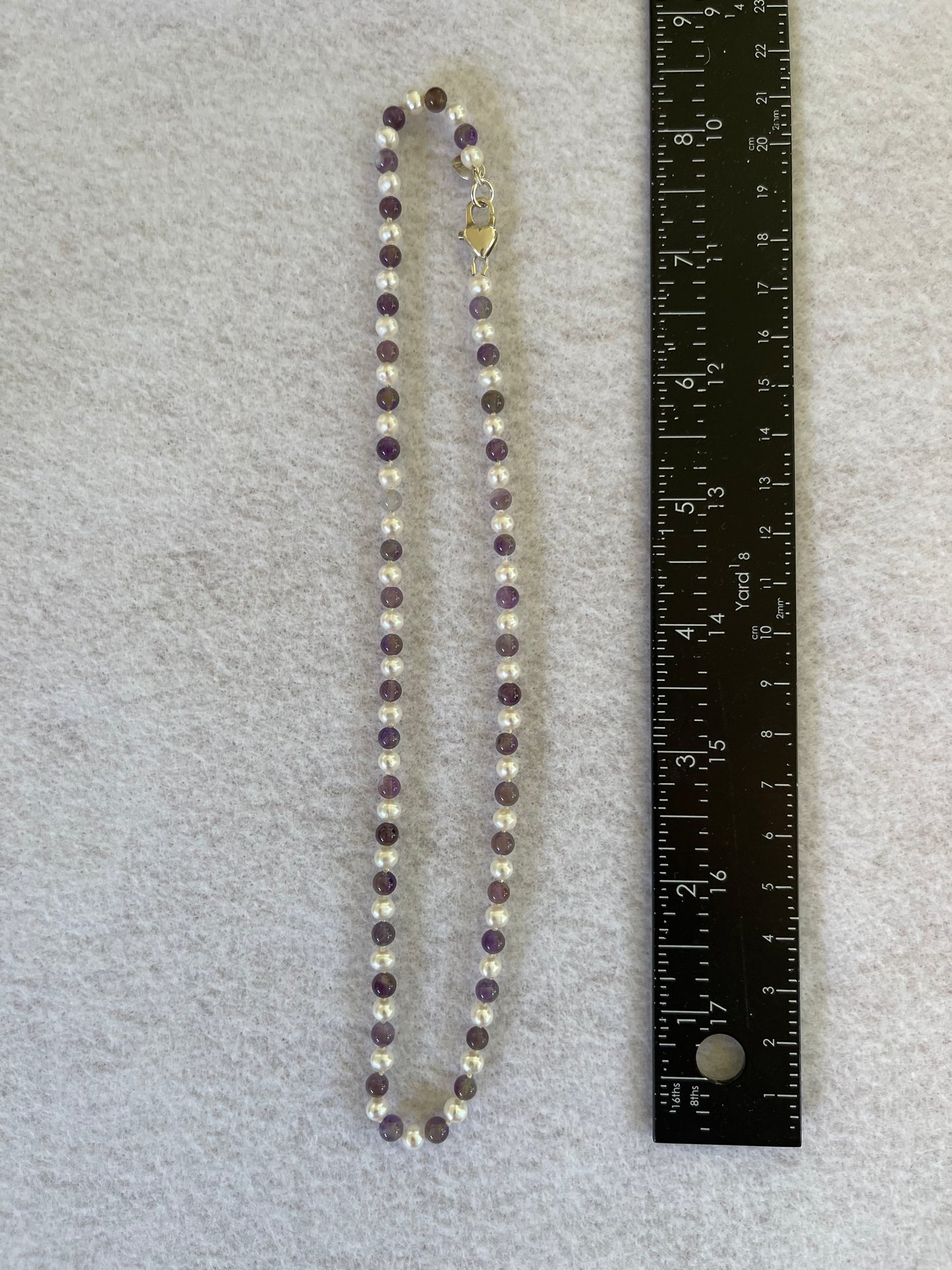 Beaded necklace with a heart-shaped pendant next to a ruler on a gray background