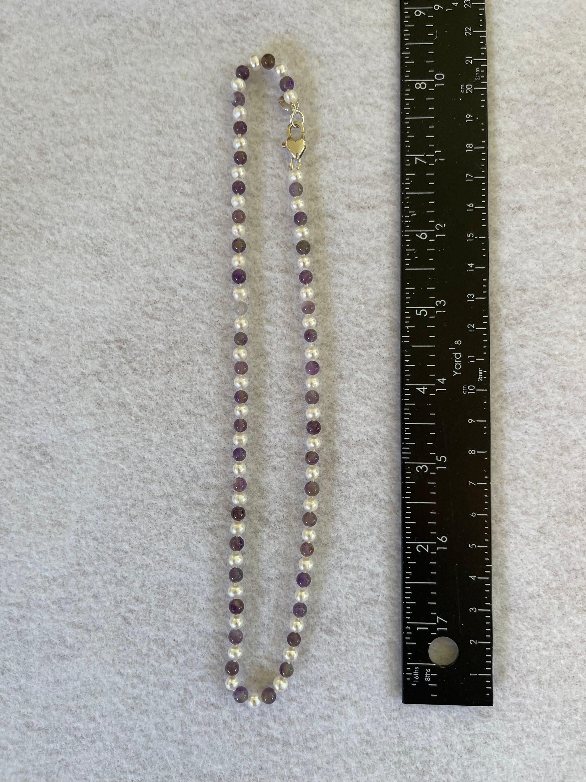 Beaded necklace with a heart-shaped pendant next to a ruler on a gray background