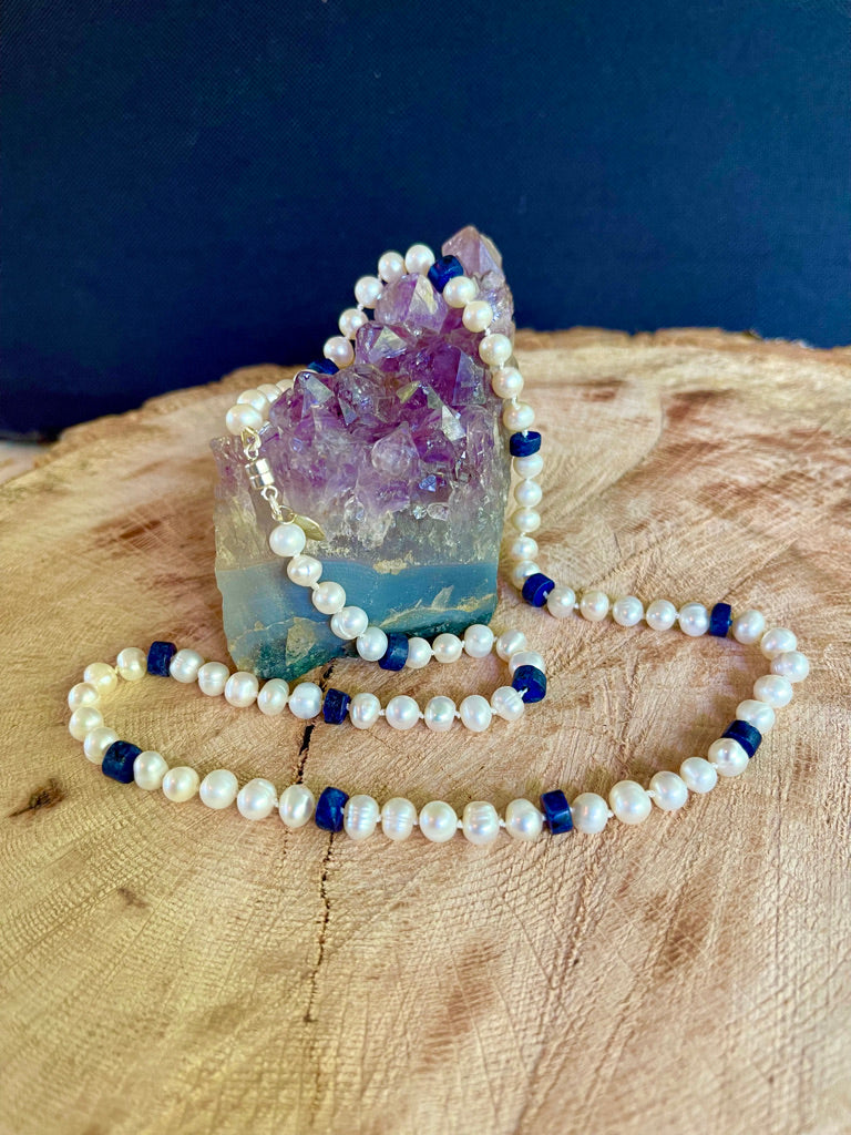 necklace  by itself with pearls and lapis lazuli on a wooden surface with an amethyst crystal.