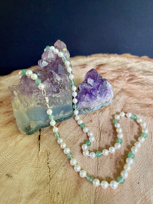 necklace of aventurine green beads and white pearls on a rock of Amethyst on a wooden board