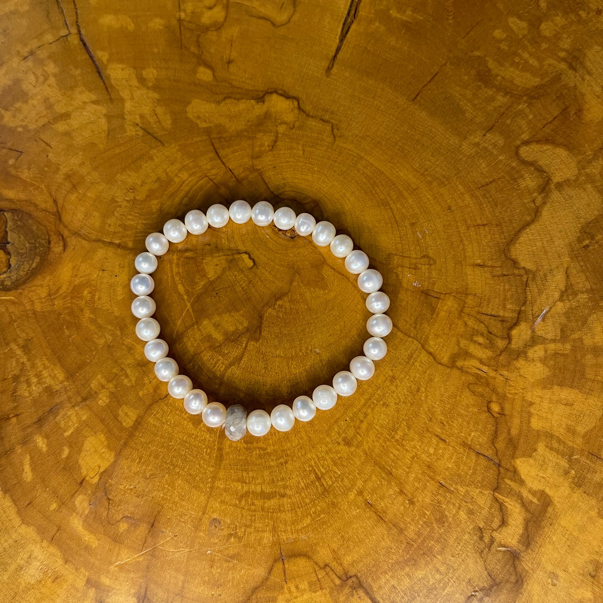 White freshwater Pearls with Grey Chalcedony Rondelle focus bead on elastic, 7 1/2" on a wooden surface