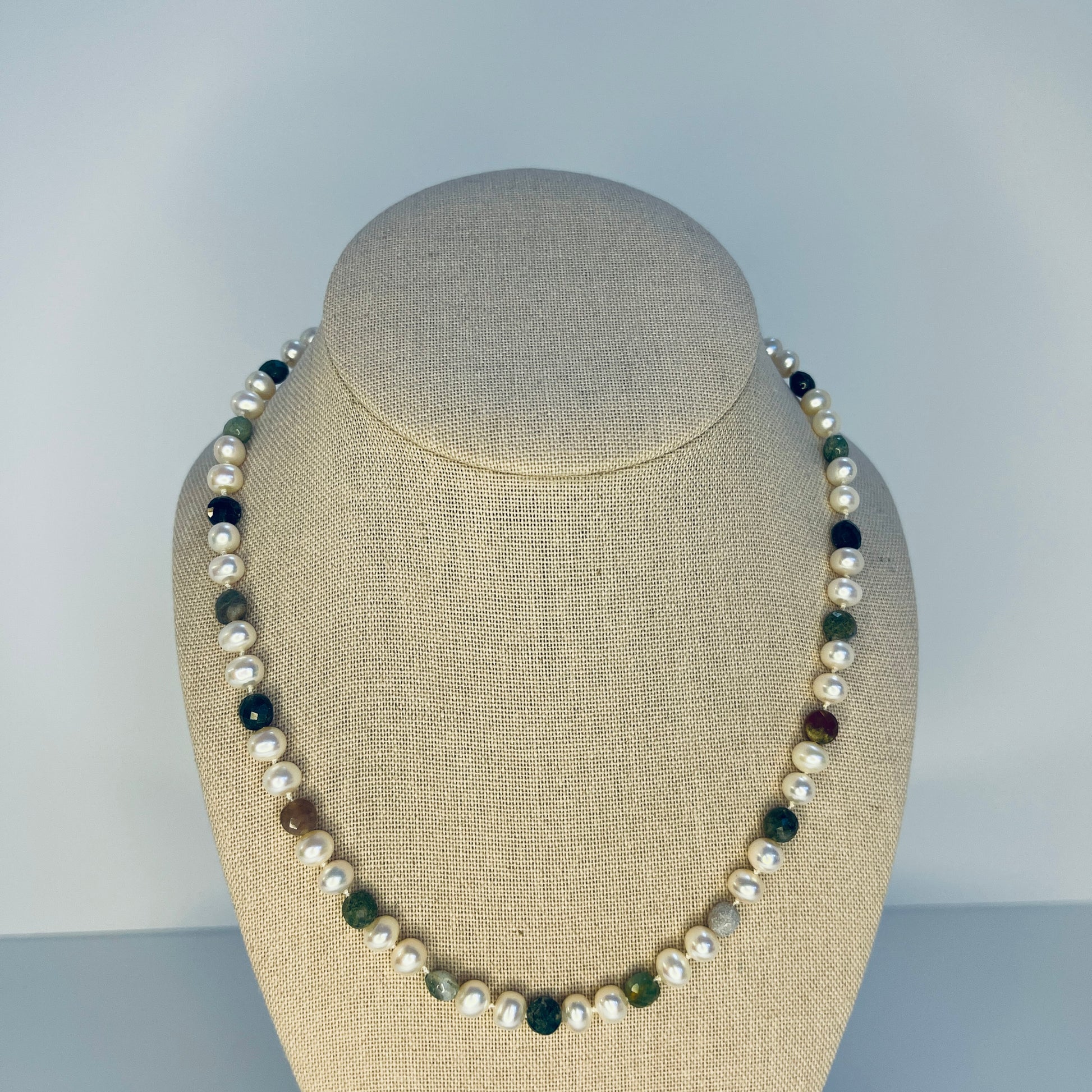 Necklace with pearls and multicolored Jasper stones on a beige bust against a gray background