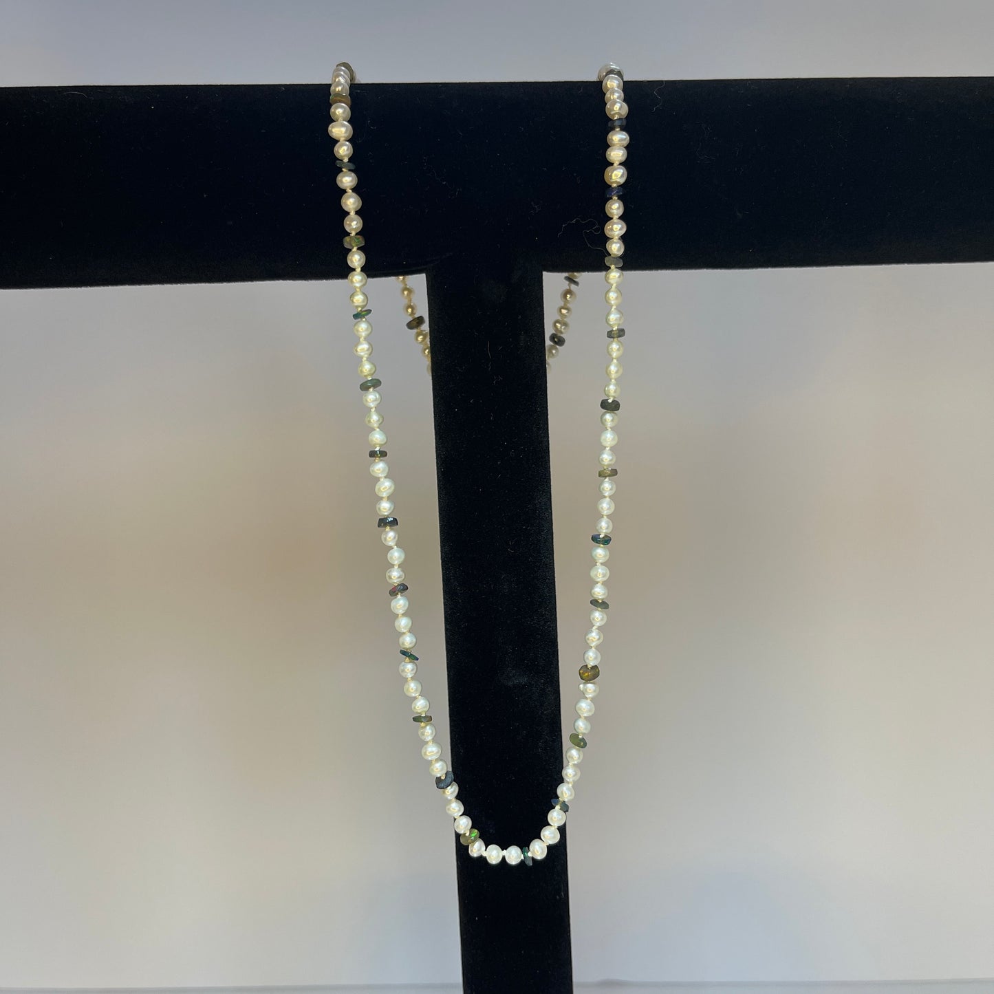 Pearl  and black opal disc necklace on a black stand against a white background