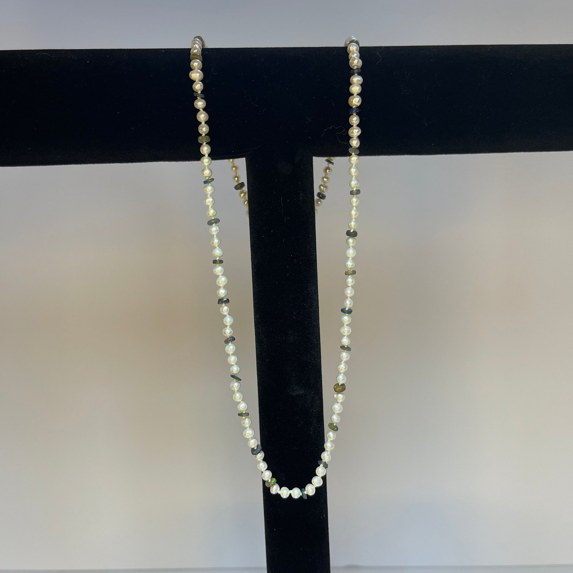 Pearl  and black opal disc necklace on a black stand against a white background