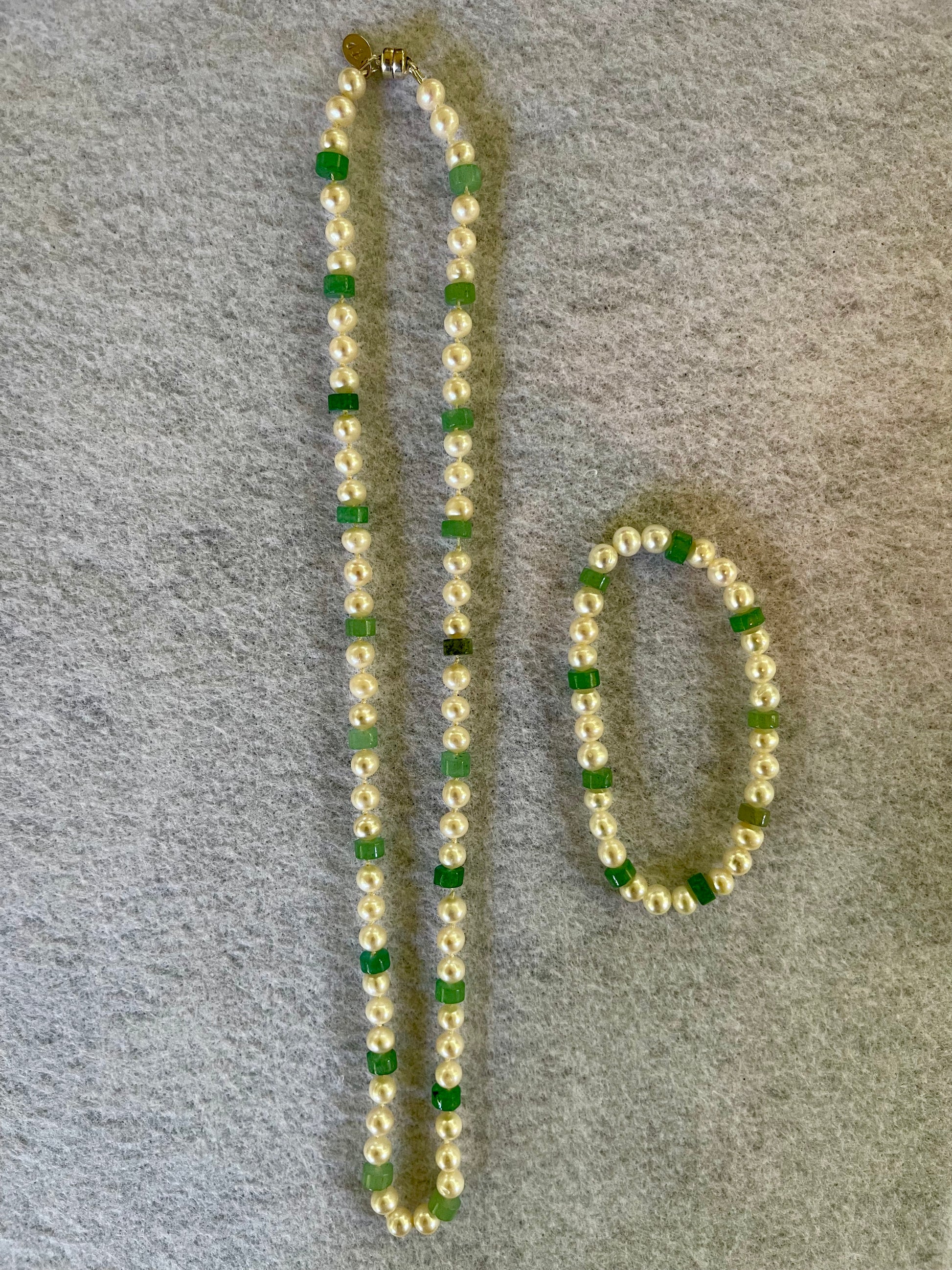 White round Pearls and Aventurine heishi discs beaded necklace and matching stretchy bracelet on a gray surface