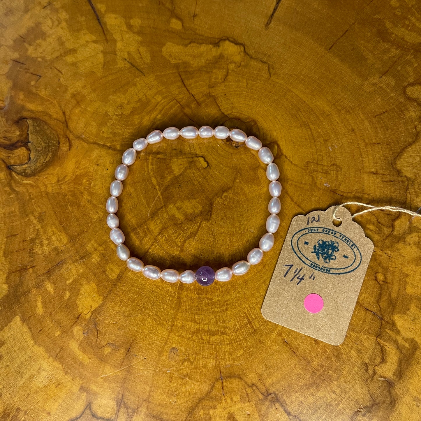 Mauve freshwater Rice  Pearls with Amethyst focus bead on elastic, 7 1/4" on a wooden surface with tag