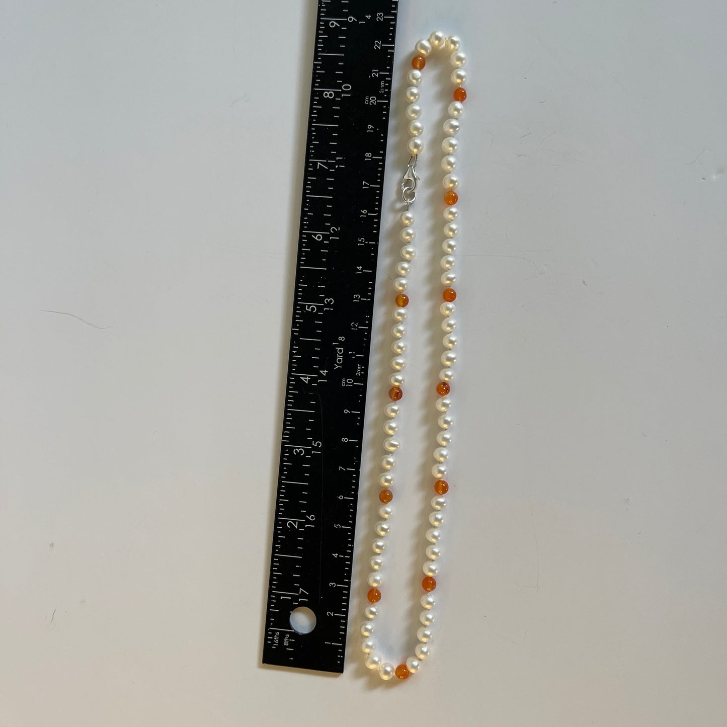 Pearl necklace with orange Carnelian beads next to a ruler on a white background