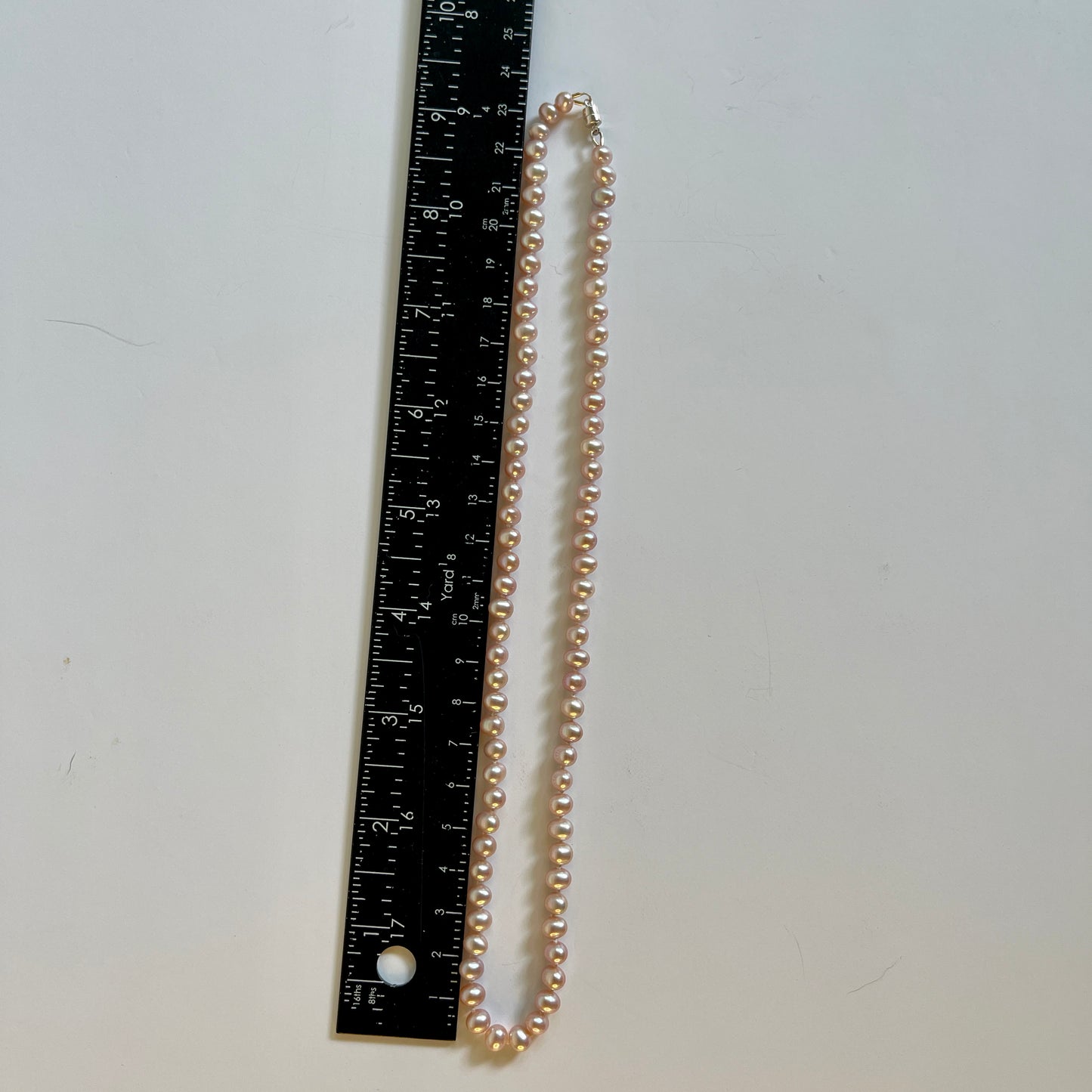 pink Pearl necklace next to a ruler on a white background