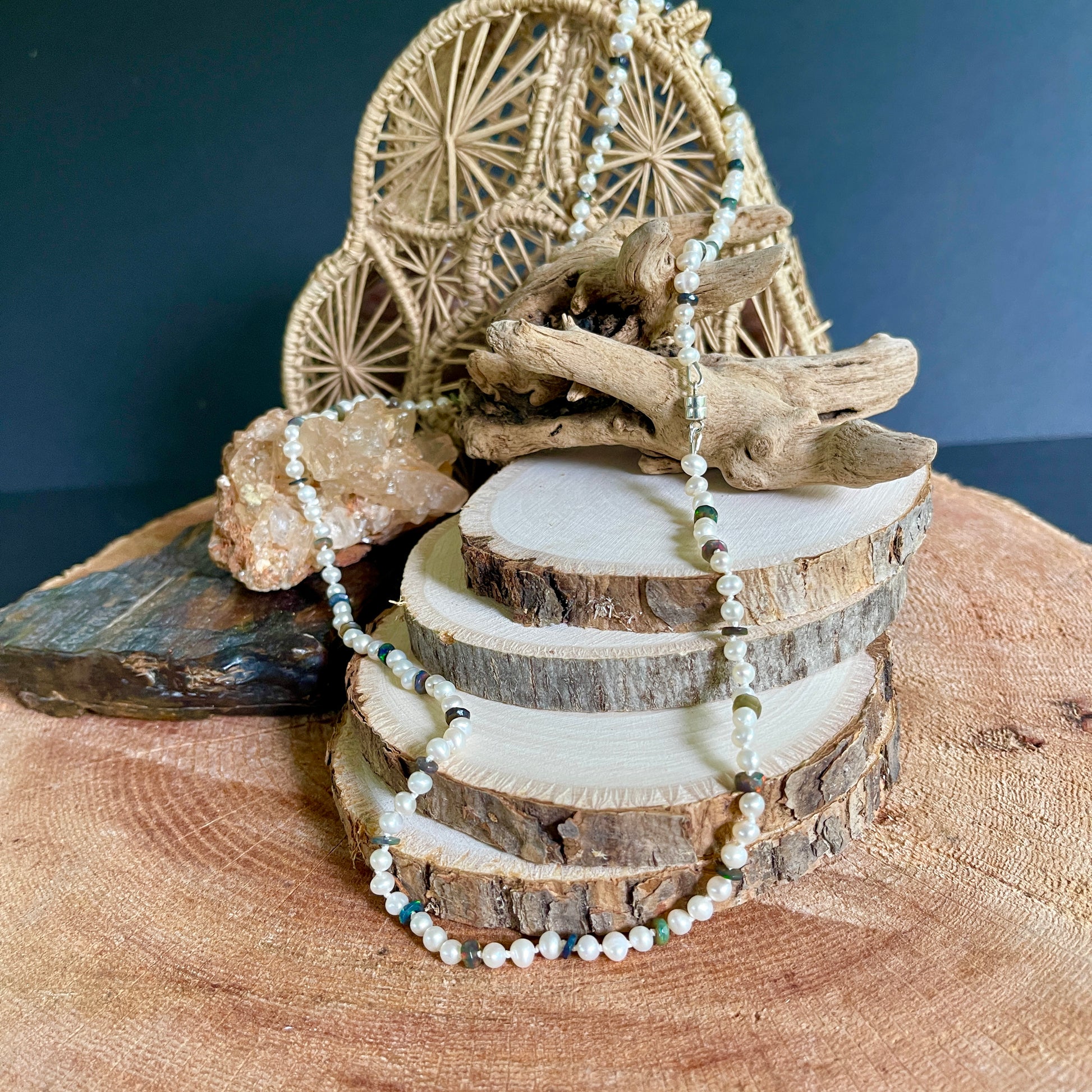 Decorative arrangement with wooden elements and a beaded  Pearl and Black Opal necklace on a dark blue background